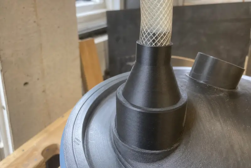 Svart 3D-printet overgang mellom en tynn slange og inntaket på en syklonutskiller på en bøtte