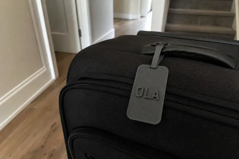 Mørkegrå 3D-printet bagasjelapp med navnet OLA på håndtaket til en svart koffert