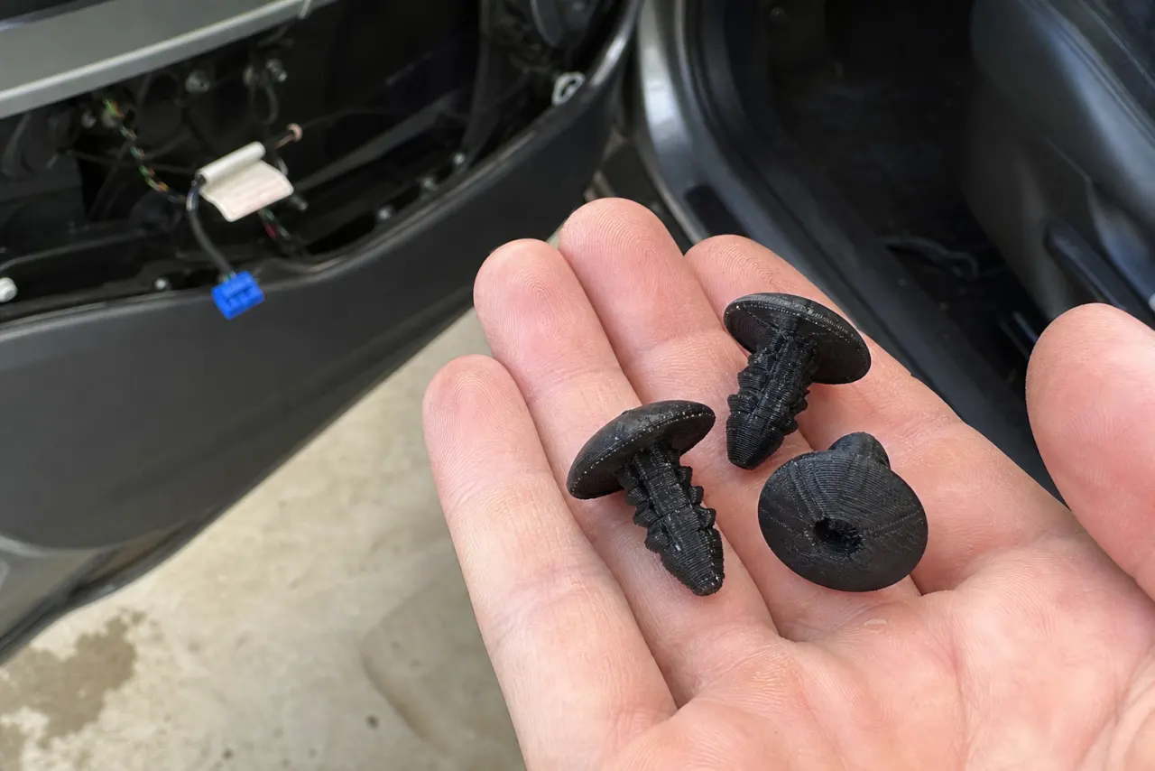 Tre svarte 3D-printede klips ved en åpen dørkledning på en bil