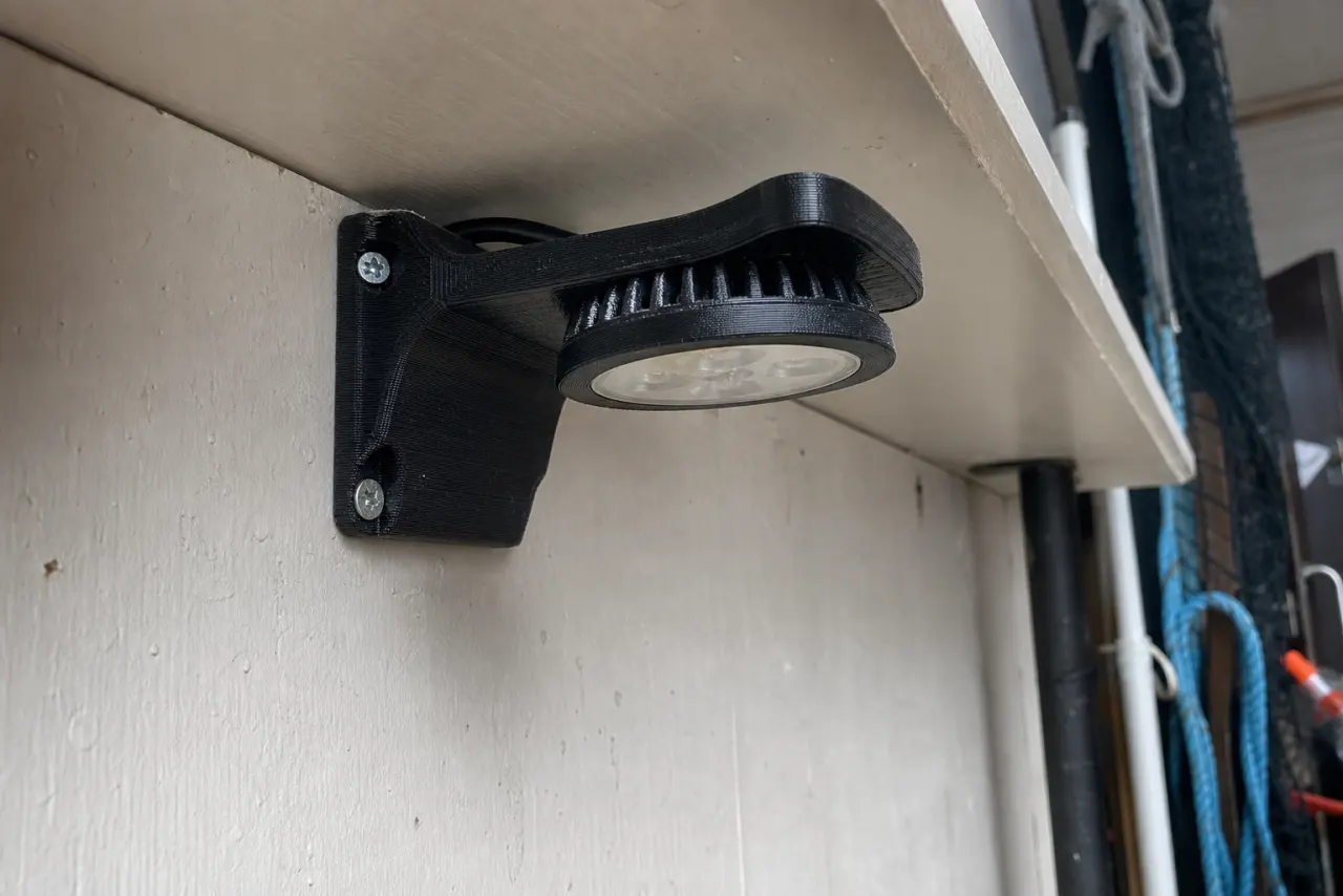 Svart 3D-printet brakett som holder en lampe under en hylle