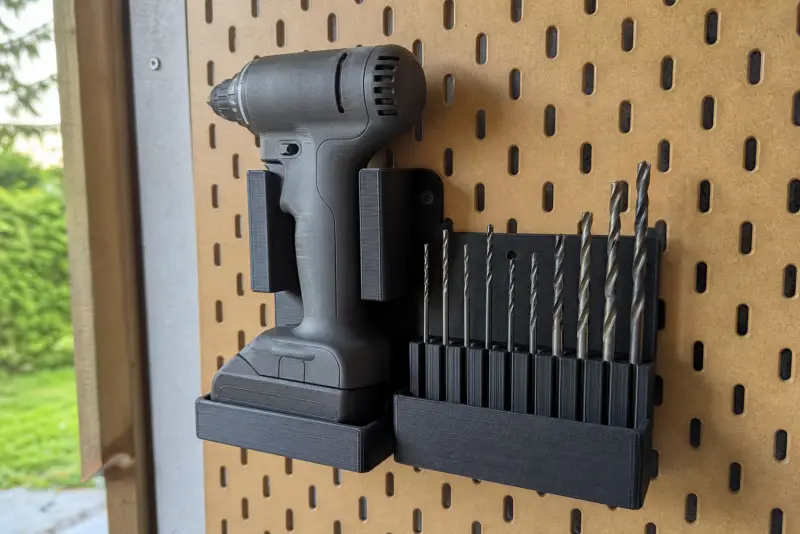 Svart 3D-printet holder med en batteridrill og en rad bits på en verktøyvegg i en garasje