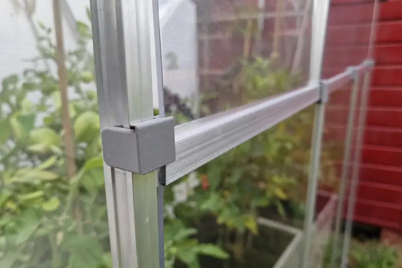 Små grå 3D-printede klips som holder en plate i aluminiumsrammen på et lite drivhus