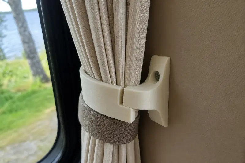 Offwhite 3D-printet gardinfeste ved et bobilvindu som holder en plissert gardin