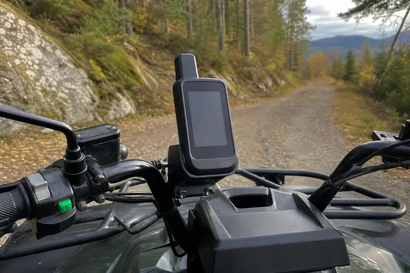 Svart 3D-printet holder med en håndholdt GPS på styret til en ATV på en skogsvei om høsten