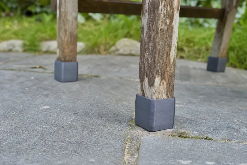 Nye grå 3D-printede føtter på beina til en værbitt hagestol av tre på steinheller
