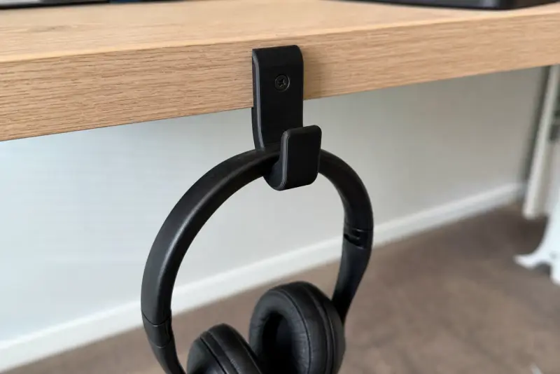 Svart 3D-printet krok under kanten av et skrivebord med et par svarte hodetelefoner