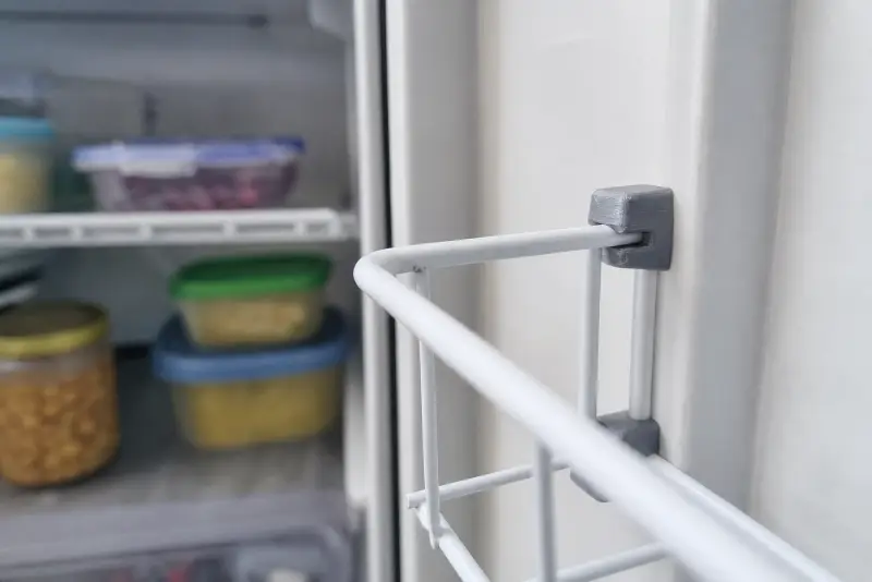 To grå 3D-printede hylleklips som holder en trådhylle i kjøleskapet i en bobil