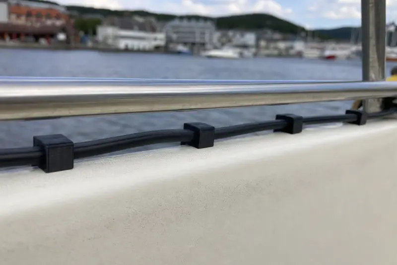 Små svarte 3D-printede klips som holder en kabel langs rekka på en småbåt