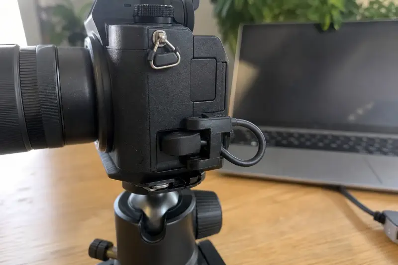 Svart 3D-printet kabelklemme på siden av et kamera på stativ som holder en USB-kabel