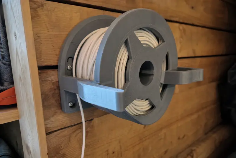 Grå 3D-printet kabelkveil på en trevegg med en lang hvit kabel kveilet rundt