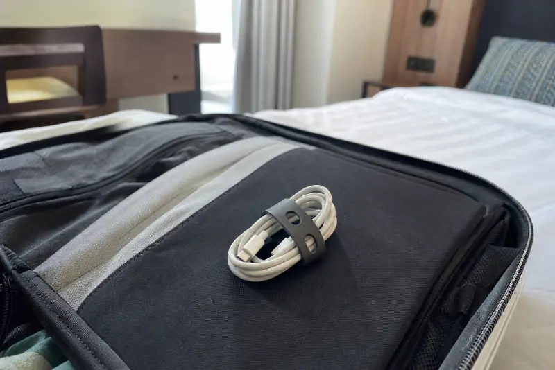 Myk mørkegrå 3D-printet kabelholder med en opprullet ladekabel på en åpen reiseveske
