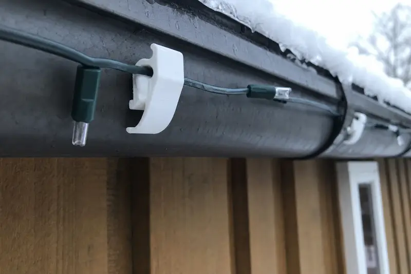 Hvite 3D-printede klips som holder en lysslynge fast i en takrenne med snø