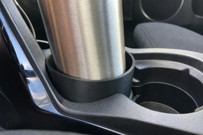 Svart 3D-printet innsats i koppholderen i en bil som holder en drikkeflaske av metall