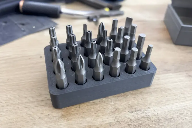Grå 3D-printet bitsholder med rader av skrutrekkerbits på en arbeidsbenk