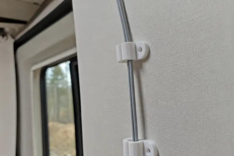 Hvite 3D-printede kabelclips som holder en grå ledning langs veggen i en bobil