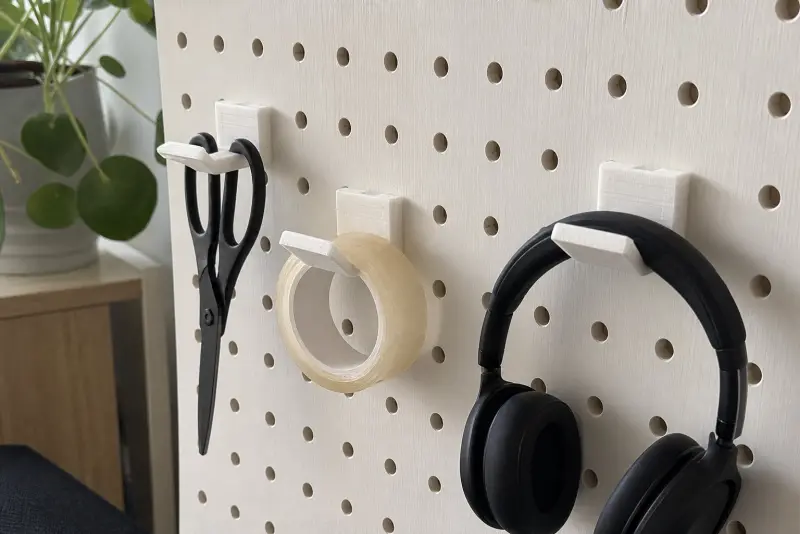 Hvite 3D-printede kroker på en hvit tavle med saks, teip og hodetelefoner