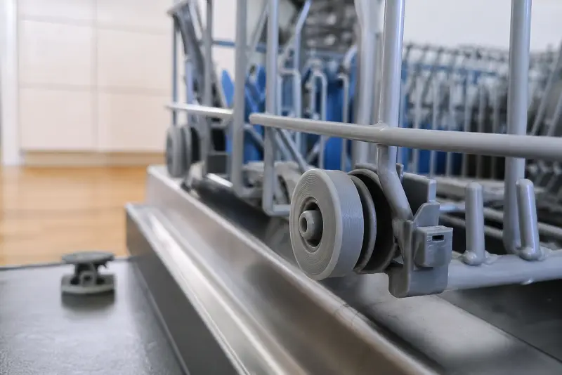 Nytt grått 3D-printet hjul på den nederste kurven i en oppvaskmaskin, det knekte hjulet på døra
