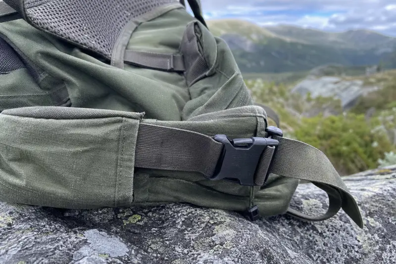 Ny svart 3D-printet spenne på hoftebeltet til en brukt tursekk på en stein i fjellet