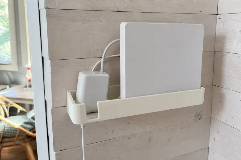 Offwhite 3D-printet veggholder med en hvit ruter og strømforsyning på en hyttevegg innendørs