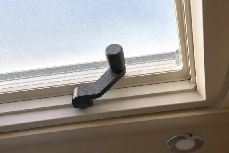 Svart 3D-printet sveivhåndtak på rammen til en takluke, sett fra innsiden av en bobil