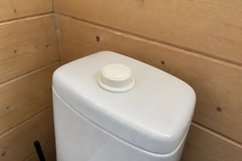 Liten offwhite 3D-printet spyleknapp på en hvit sisterne på et hyttebad med panel