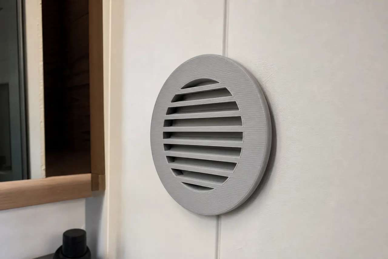 Lysegrå 3D-printet rund ventilasjonsrist på en hvit vegg på et hyttebad