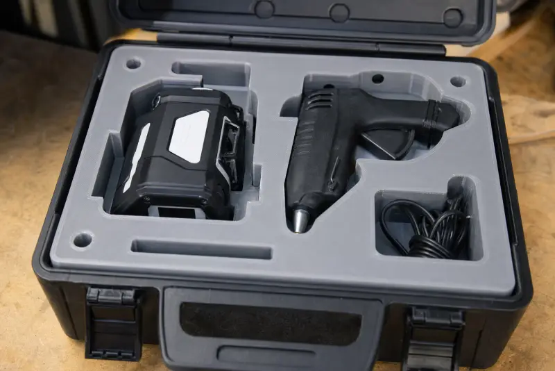 Åpen verktøykasse med en grå 3D-printet innsats som holder en krysslaser og en limpistol